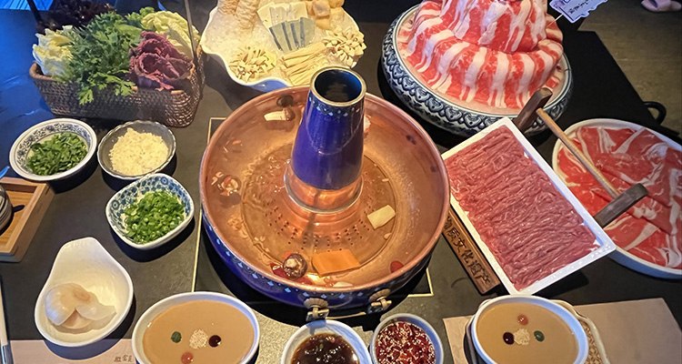A copper hotpot surrounded by sliced meat and side dishes